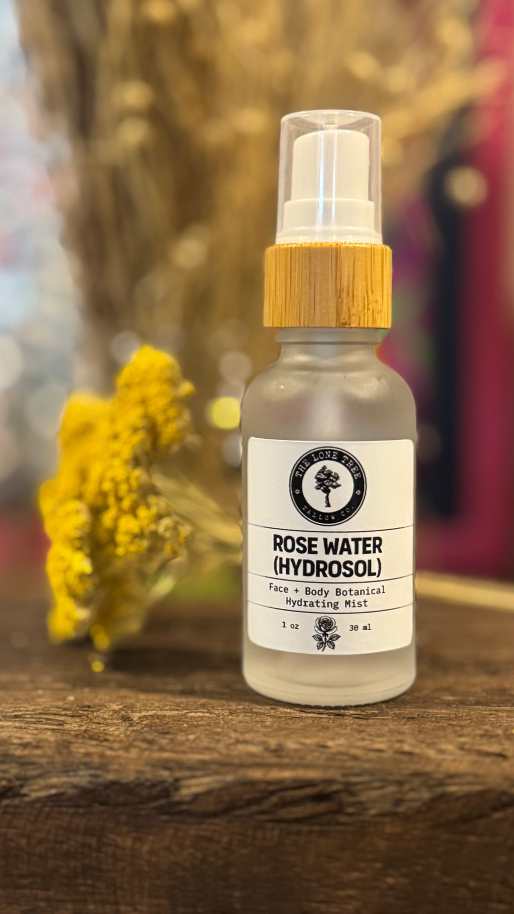 rose water hydrosol in a 1 oz frosted white glass spray jar on a wooden beam next to dried yarrow. 