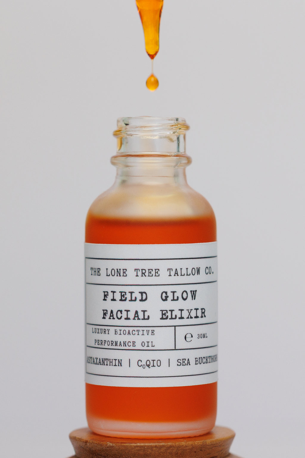 1 oz bottle of Field Glow luxury facial Elixir with a droplet of the orange/gold oil dropping into the bottle on a white background. contains astaxanthin, CoQ10, sea buckthorn and teprenone. compare to vintner's daughter or Oliver Midy luxury oils. 