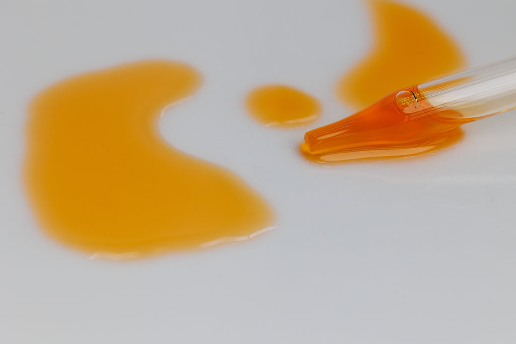 The Field Glow Facial Oil Elixir being dripped from a dropper onto a white surface showing the beautiful orange glow of the oil that contains sea buckthorn, astaxanthin, CoQ10, and teprenone. 