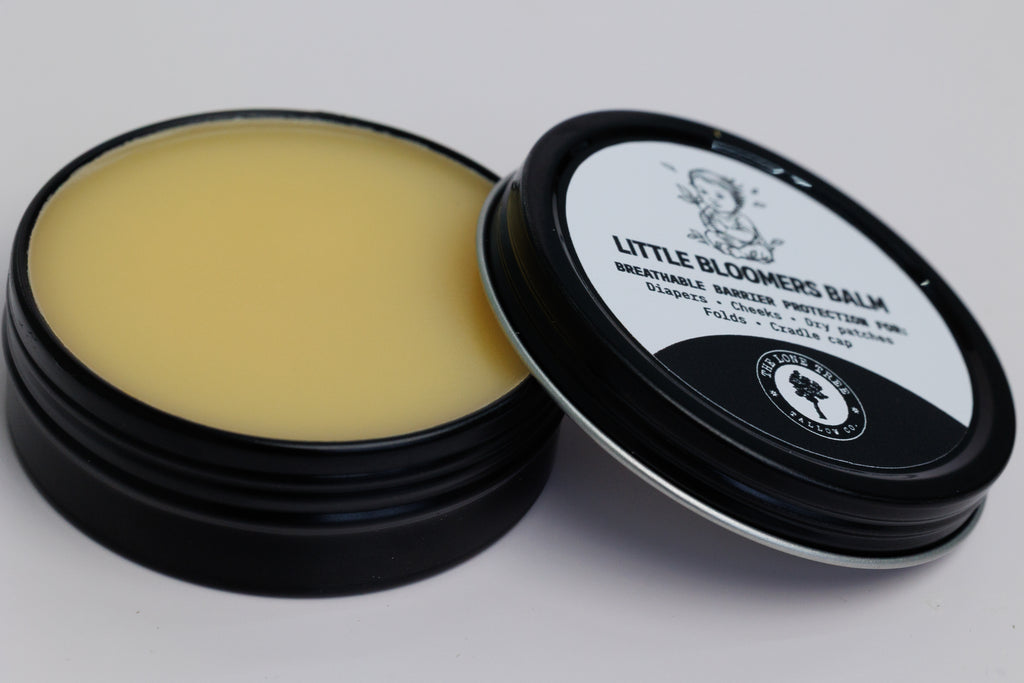 Open jar showing texture and color of Little Bloomers Balm from Lone Tree Tallow Co. in a 2 oz black tin. used for diapers, cradle cap and dry patches. safe for babies. pure heritage tallow, calendula infused sunflower oil, vitamin E. no essential oils. pure and natural. 