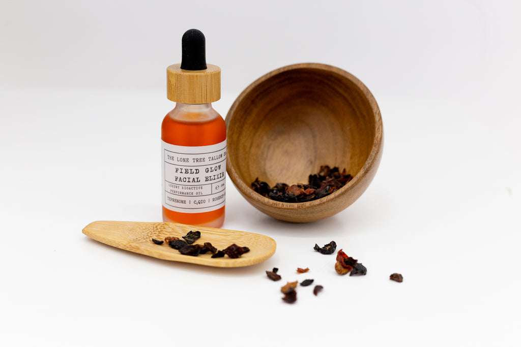 Lone Tree Tallow Field Glow Luxury Facial Oil Elixir with Astaxanthin, sea buckthorn & CoQ10 sitting next to a wooden bowl with rosehips and a wooden spoon. 