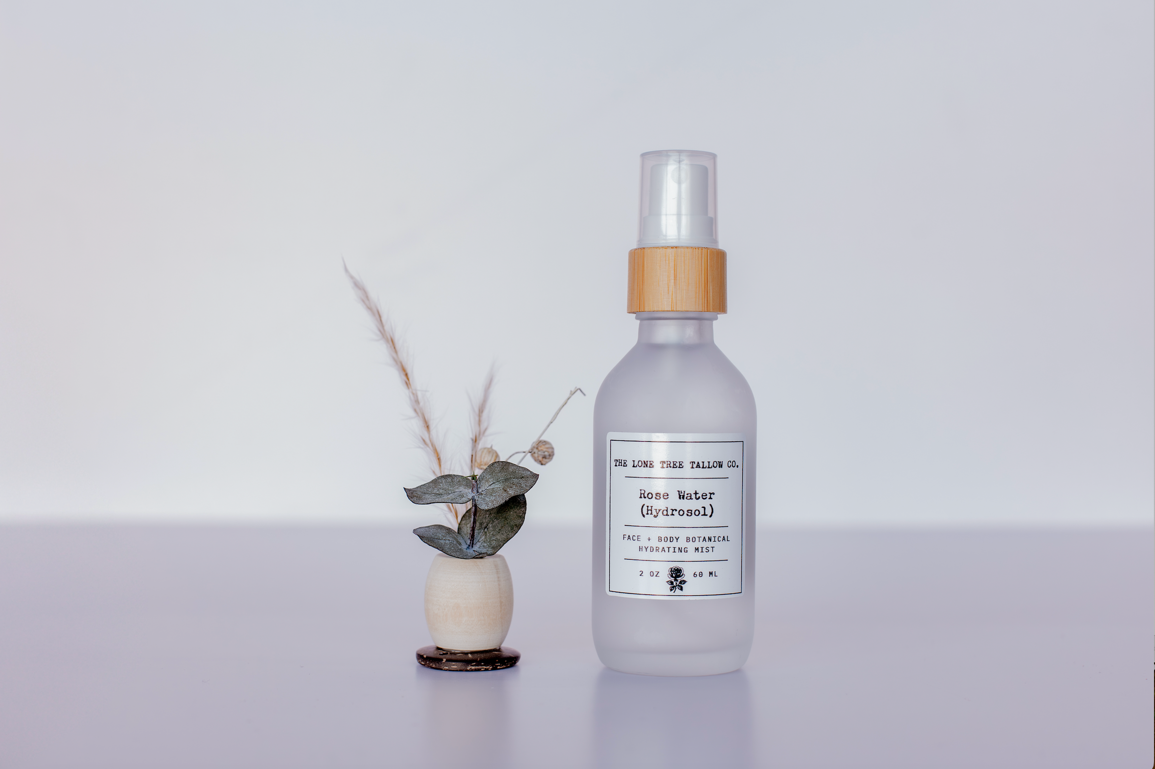 a picture of rose water (hydrosol) in a 2 oz glass jar next to a small flower in a wooden bead. lone tree tallow co. 