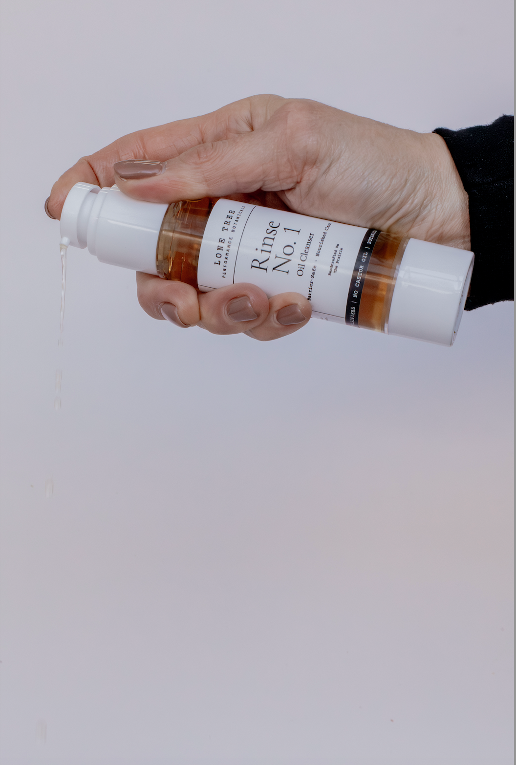 Rinse No. 1 Oil Cleanser does not strip your skin's natural barrier and is great for perimenopausal, menopausal, or hormonal skin.  This picture shows a 2oz container being held in a hand and dispensed with the forefinger.  No castor oil, emulsifers, or fragrances. Just luxury oils that melt away makeup and dirt, leaving skin feeling soft and clean. 